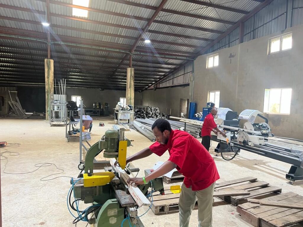The Rotex factory floor in Nigeria, a worker at a cutting machine with further machinery and lengths of profile behind him
