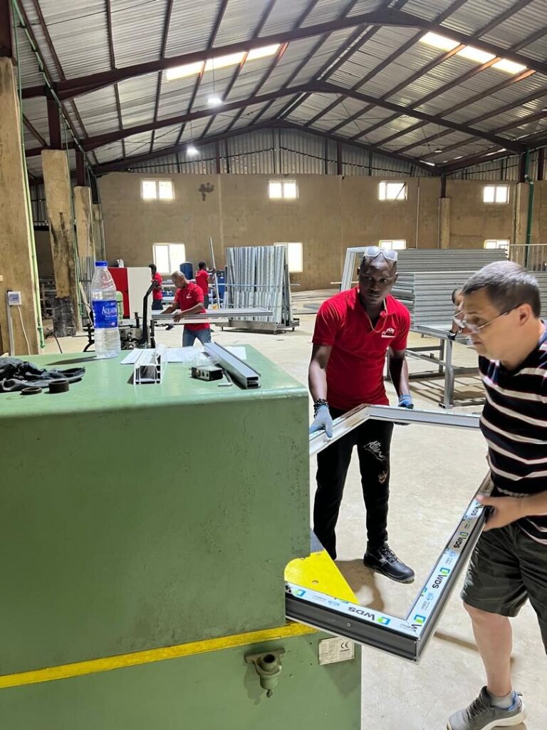Two people lifting a freshly welded white uPVC window frame off the machine at the Rotex factory