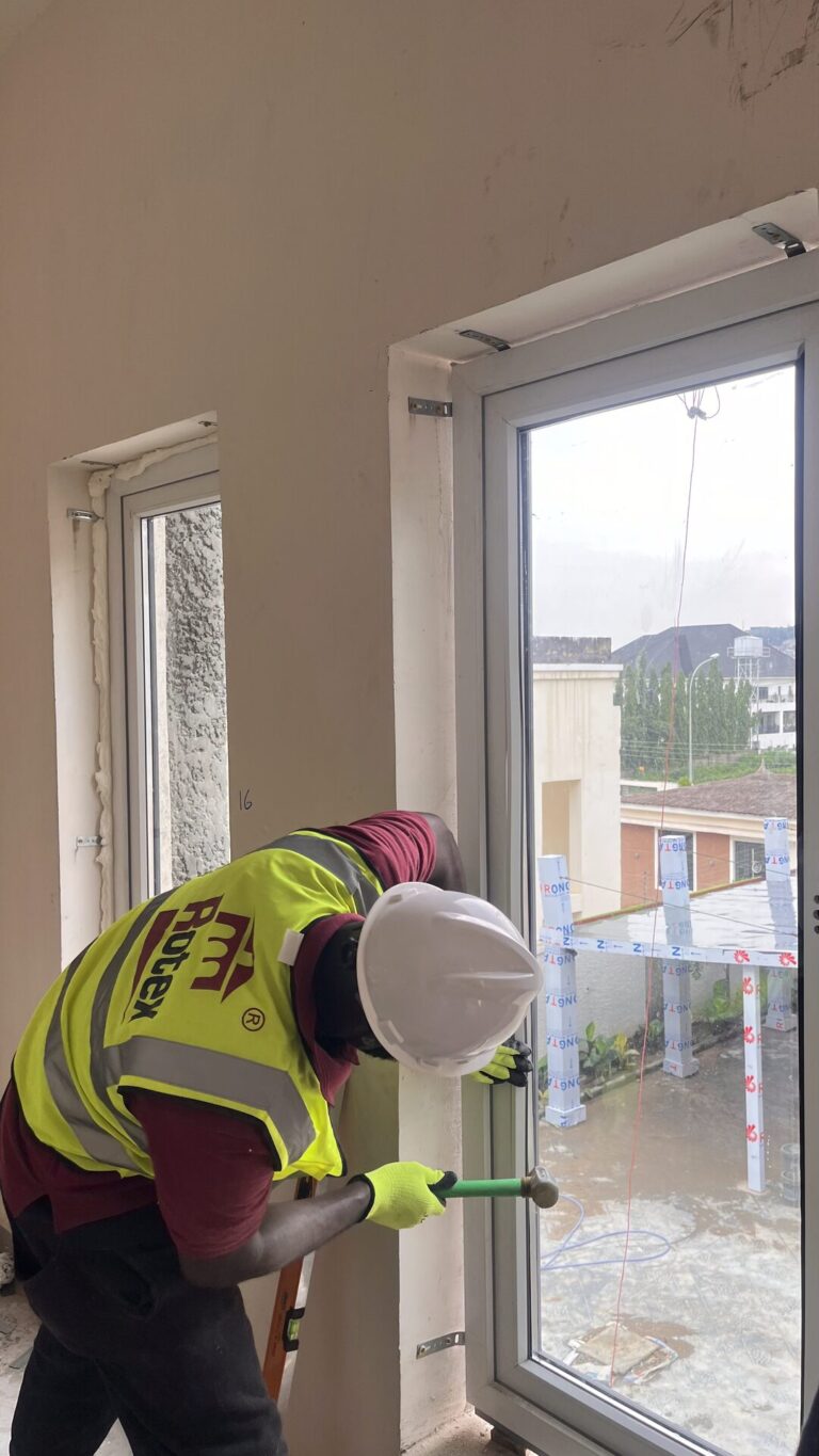 A Rotex installer lifting a sealed glazing unit into a fitted window frame