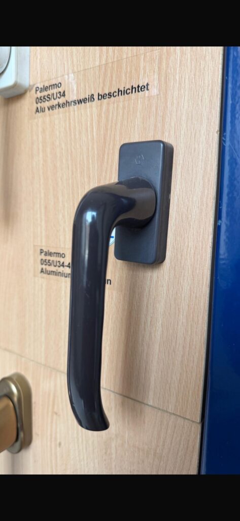 A dark grey Palermo lever handle on a showroom sample board, beside its label
